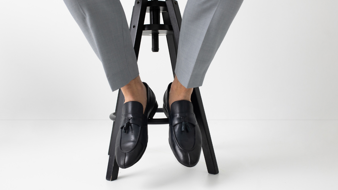 man is sleep trouser and pointy toe shoes sitting on a stool